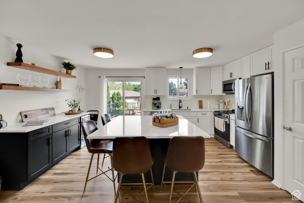 Kitchen featuring stainless steel appliances, a kitchen bar, light wood finished floors, light countertops, and tasteful backsplash