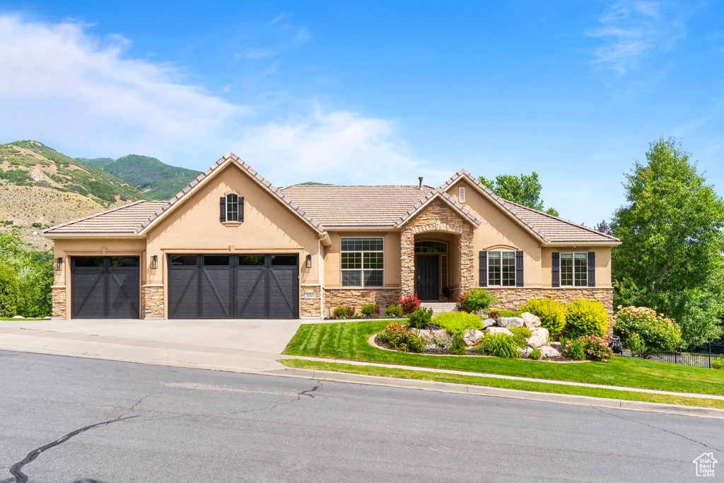 View of front facade featuring stucco siding, stone siding, an attached garage, driveway, and a mountain view