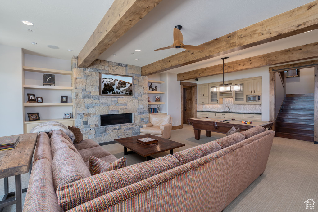 Living area with light colored carpet, beamed ceiling, a stone fireplace, a ceiling fan, and pool table