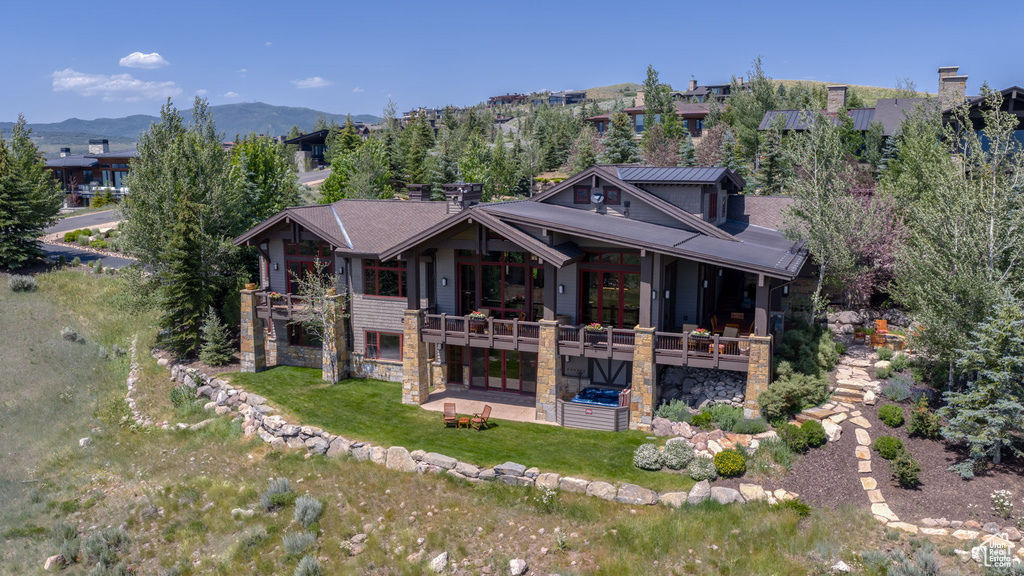 Rear view of house featuring a balcony, a patio area, stone siding, a lawn, and a mountain view
