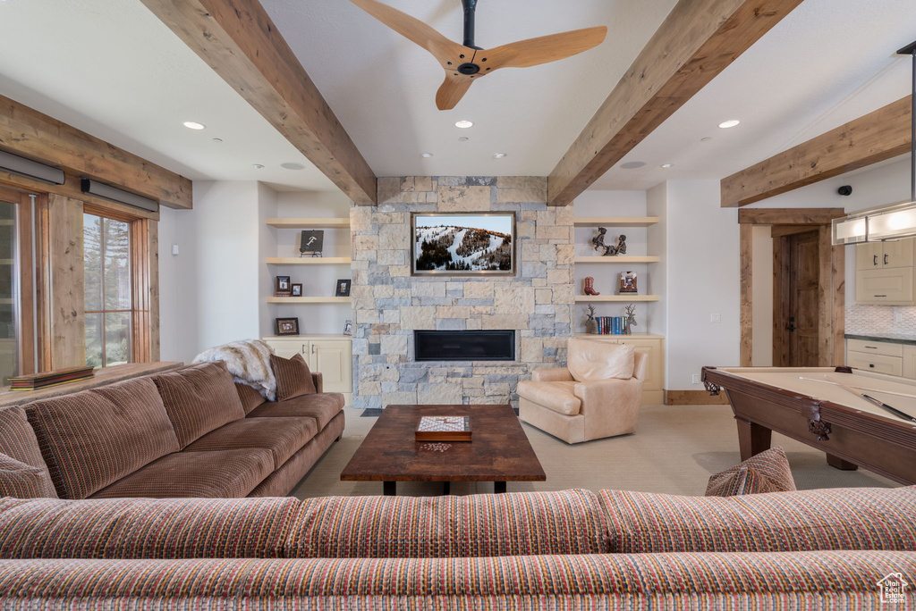 Living area featuring beamed ceiling, a ceiling fan, a stone fireplace, light colored carpet, and recessed lighting