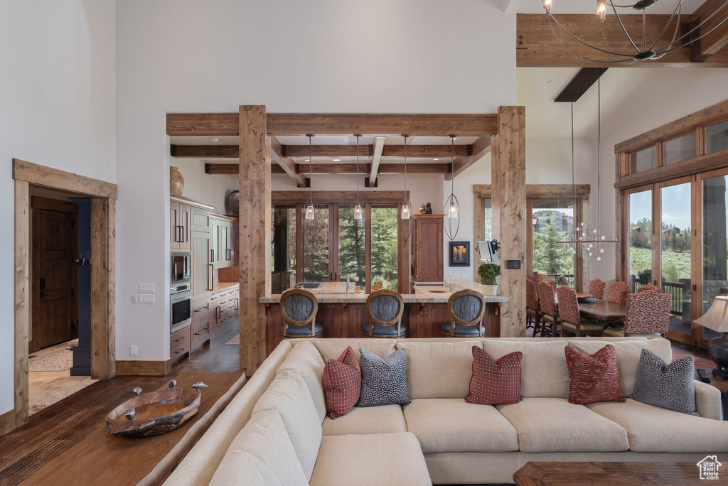 Living room with dark wood-type flooring, beam ceiling, a towering ceiling, and a chandelier