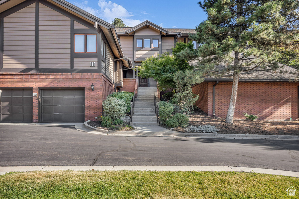 Multi unit property featuring brick siding, asphalt driveway, an attached garage, and stairway