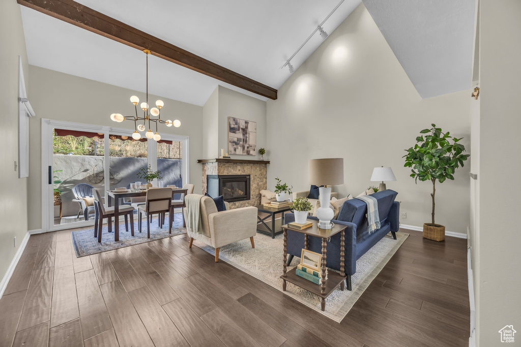 Living area with dark wood-style floors, a chandelier, a glass covered fireplace, beam ceiling, and high vaulted ceiling