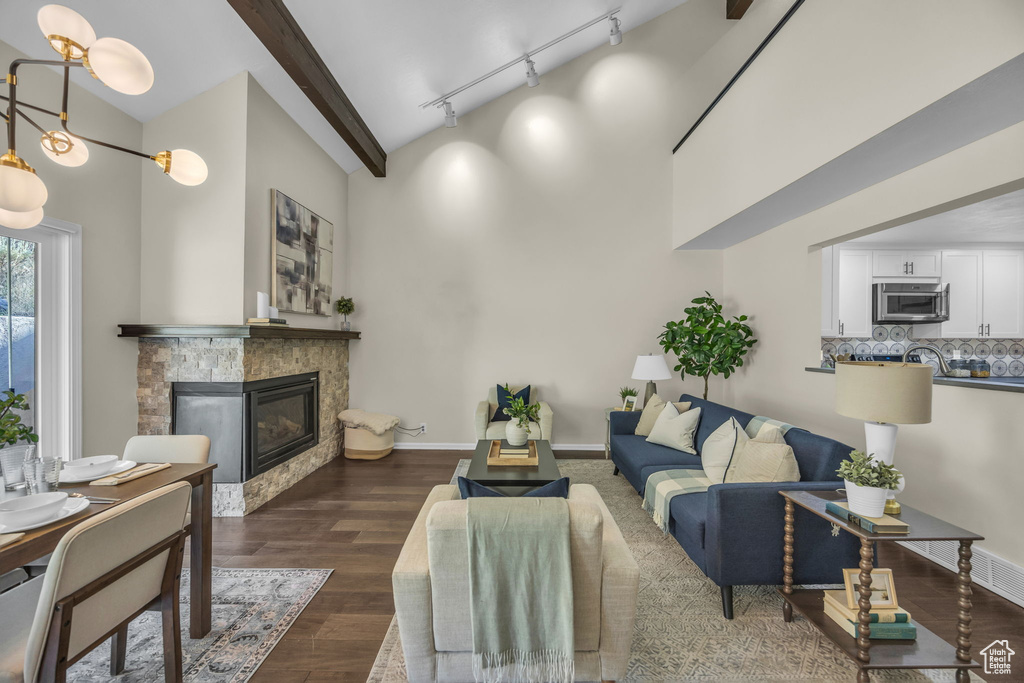 Living area featuring a glass covered fireplace, dark wood-style floors, track lighting, a towering ceiling, and beamed ceiling