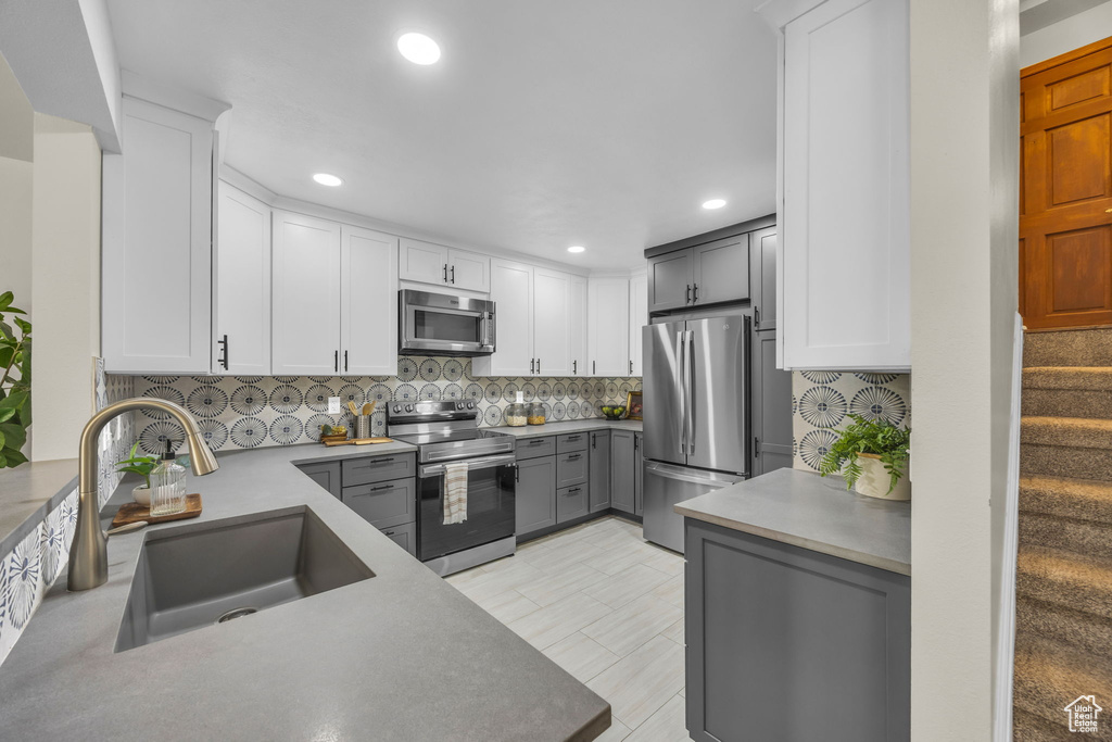 Kitchen featuring stainless steel appliances, gray cabinets, decorative backsplash, recessed lighting, and white cabinetry