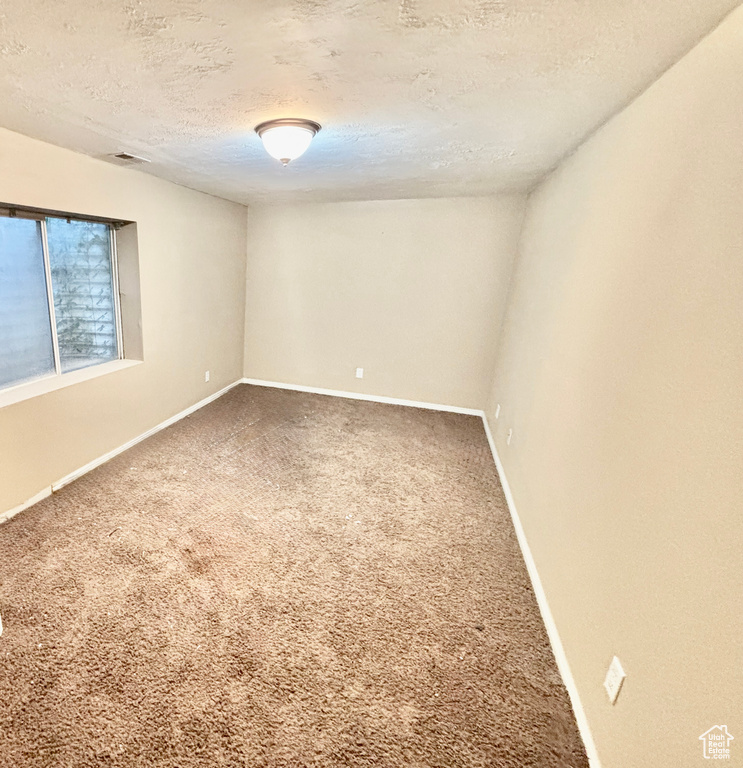 Carpeted empty room with a textured ceiling and baseboards