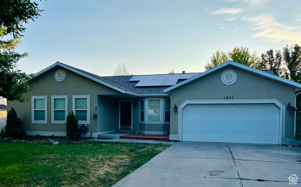 Ranch-style house featuring stucco siding, driveway, an attached garage, a front yard, and roof mounted solar panels