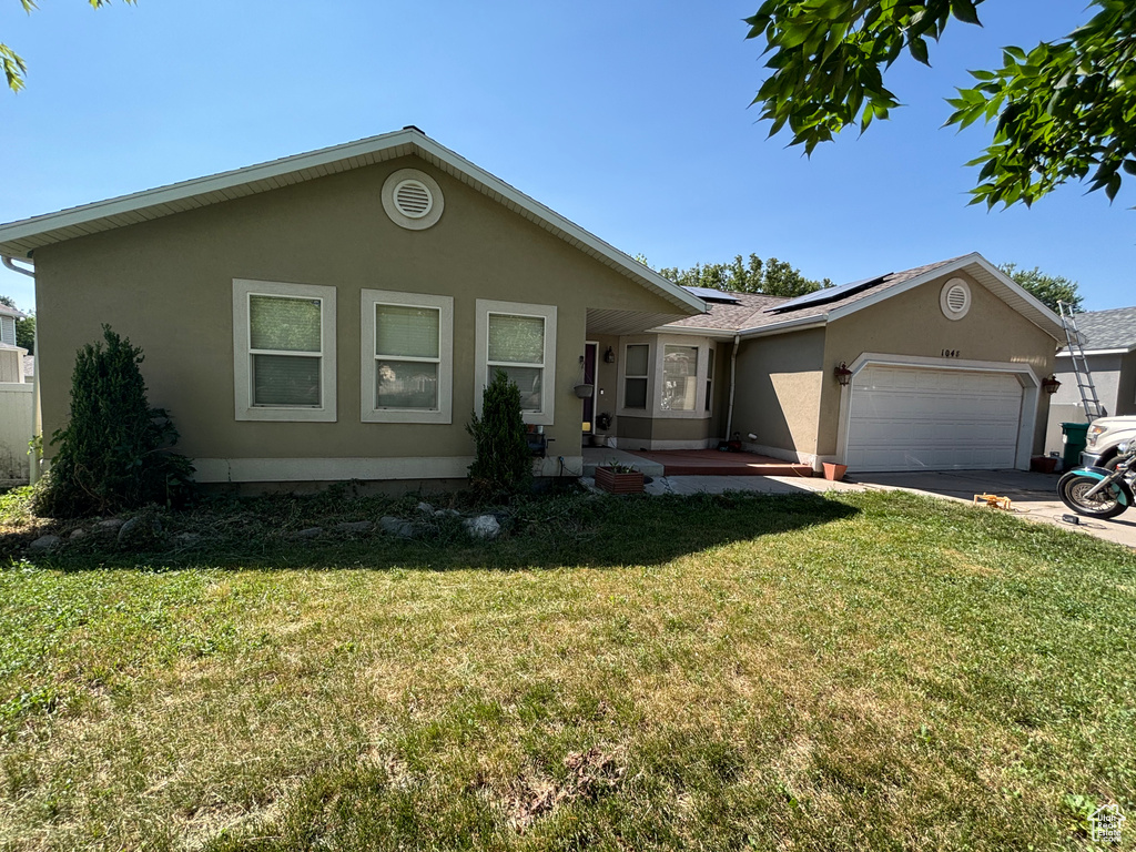 Ranch-style home featuring a garage, stucco siding, roof mounted solar panels, a front yard, and concrete driveway