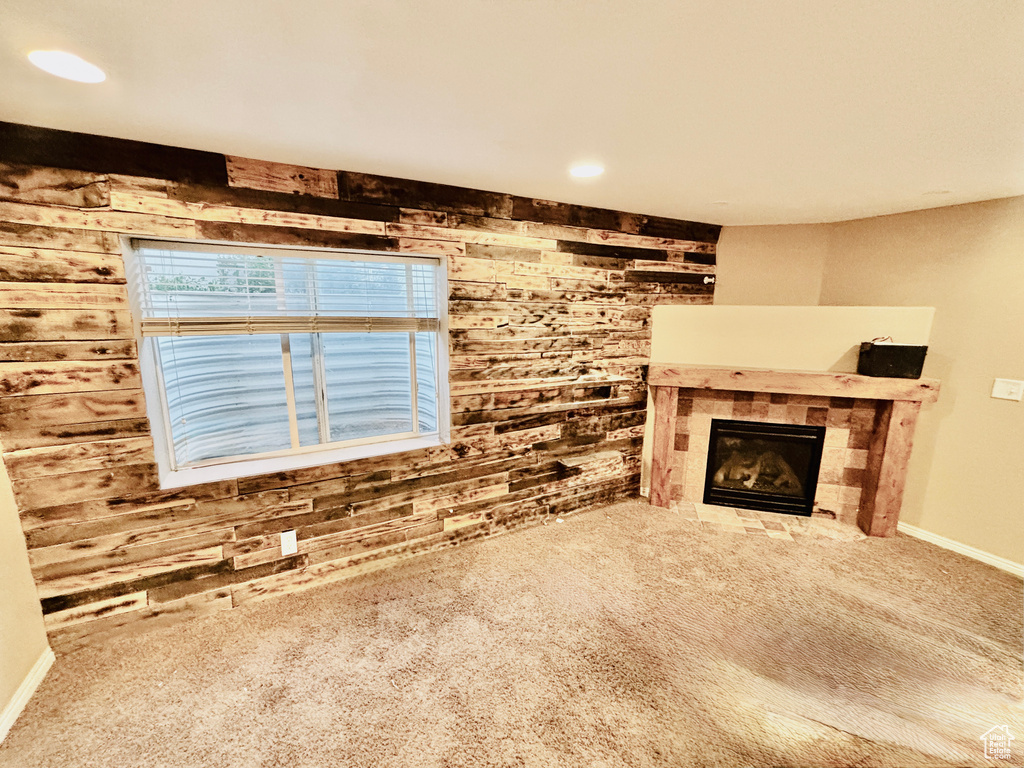 Unfurnished living room featuring wood walls, carpet flooring, and a tiled fireplace