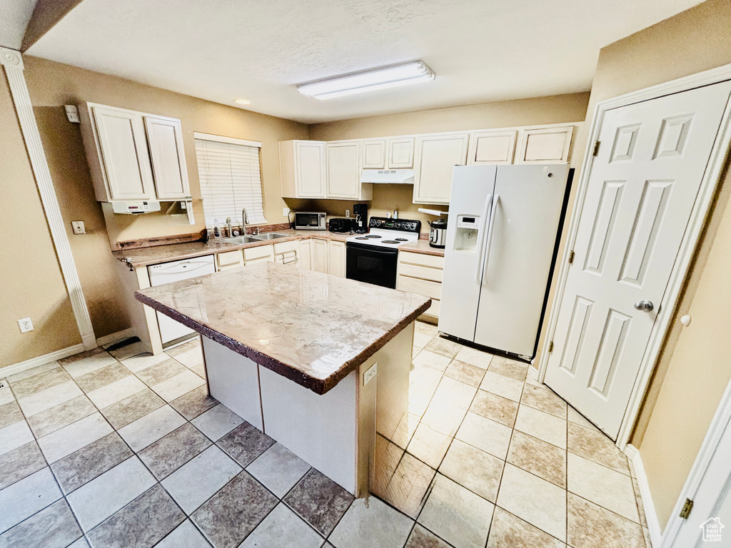 Kitchen featuring white appliances, under cabinet range hood, a kitchen island, white cabinets, and light countertops