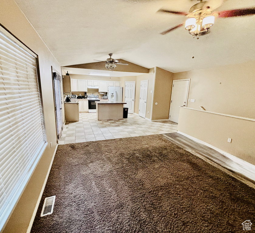 Unfurnished living room featuring ceiling fan, vaulted ceiling, light carpet, and light tile patterned flooring