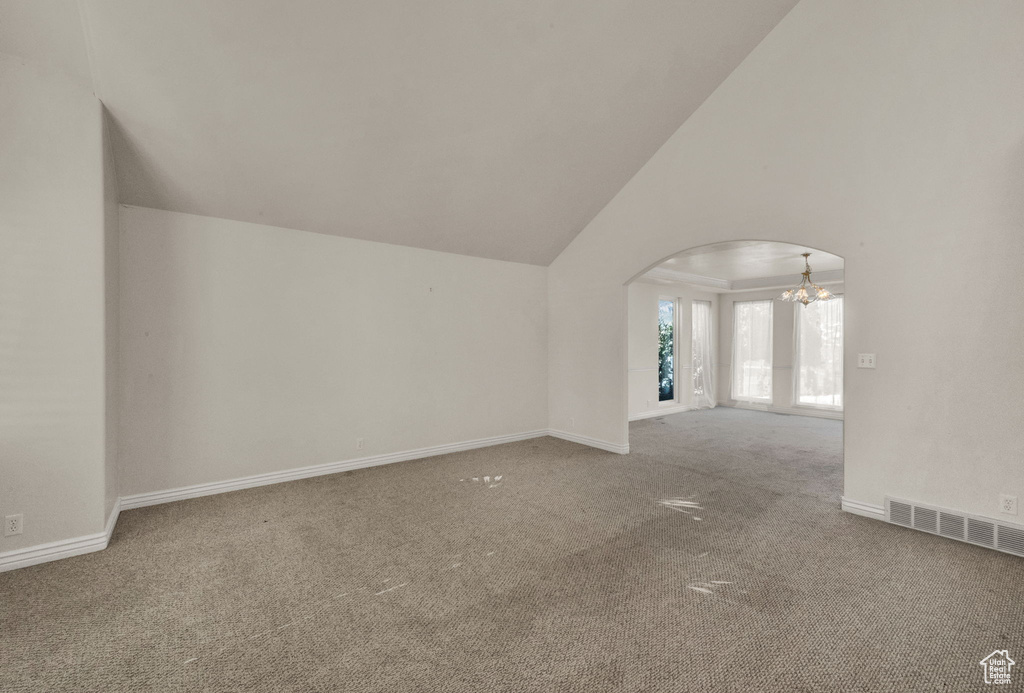 Additional living space with a chandelier, carpet, arched walkways, and high vaulted ceiling