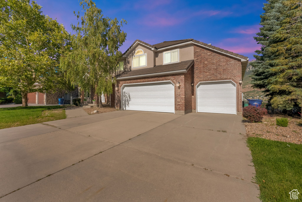 View of front facade featuring driveway, a tile roof, and a garage
