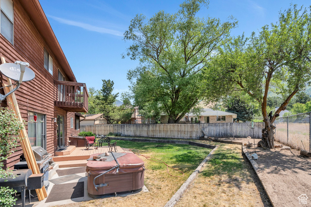 Fenced backyard featuring a hot tub, a balcony, and a wooden deck