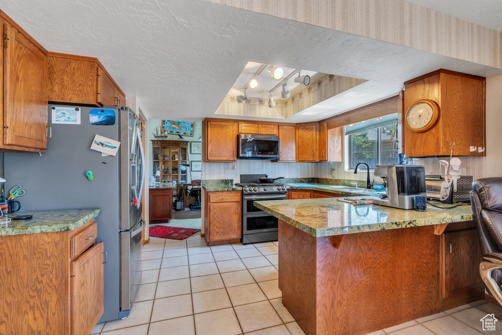 Kitchen with stainless steel appliances, a peninsula, brown cabinets, a tray ceiling, and a textured ceiling