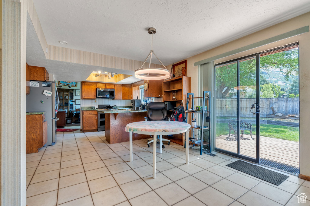 Kitchen featuring stainless steel appliances, brown cabinets, a textured ceiling, a peninsula, and light tile patterned floors