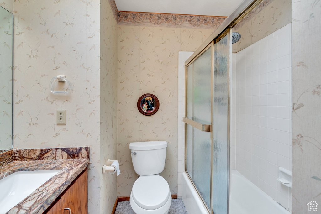 Bathroom featuring wallpapered walls, vanity, and bath / shower combo with glass door