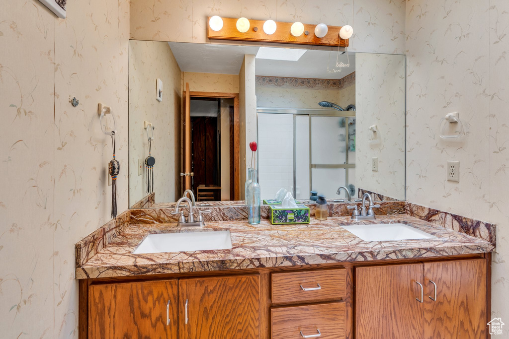 Bathroom featuring wallpapered walls, double vanity, and a stall shower