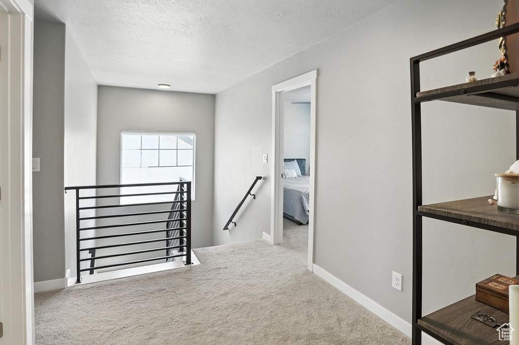 Corridor with an upstairs landing, carpet floors, and a textured ceiling