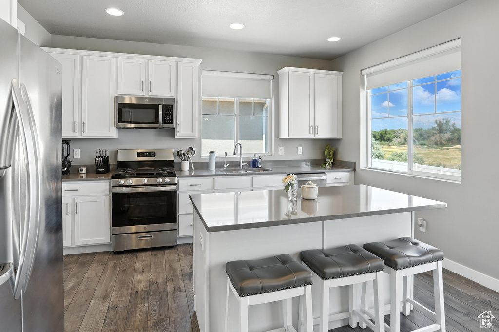 Kitchen featuring appliances with stainless steel finishes, dark wood-style flooring, a kitchen breakfast bar, white cabinetry, and recessed lighting