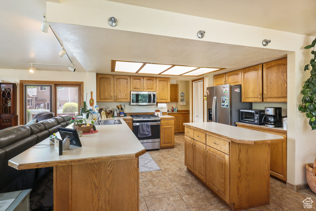 Kitchen with stainless steel appliances, light countertops, a peninsula, open floor plan, and a kitchen island