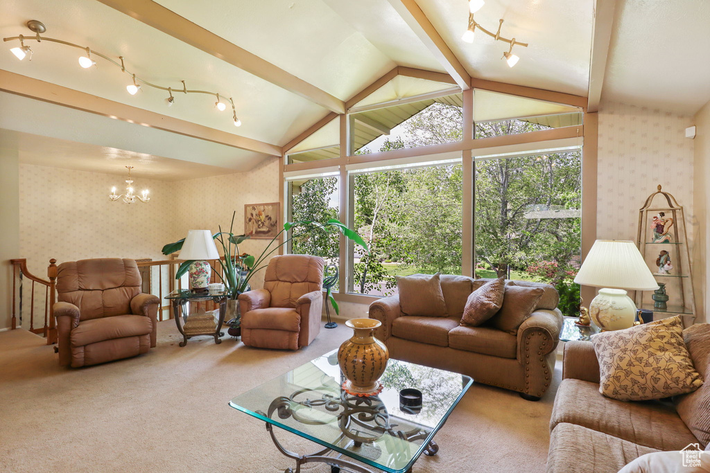 Living room featuring wallpapered walls, carpet flooring, a chandelier, vaulted ceiling, and rail lighting