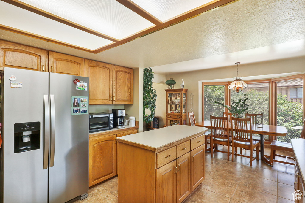 Kitchen featuring stainless steel fridge with ice dispenser, a center island, decorative light fixtures, light countertops, and brown cabinets