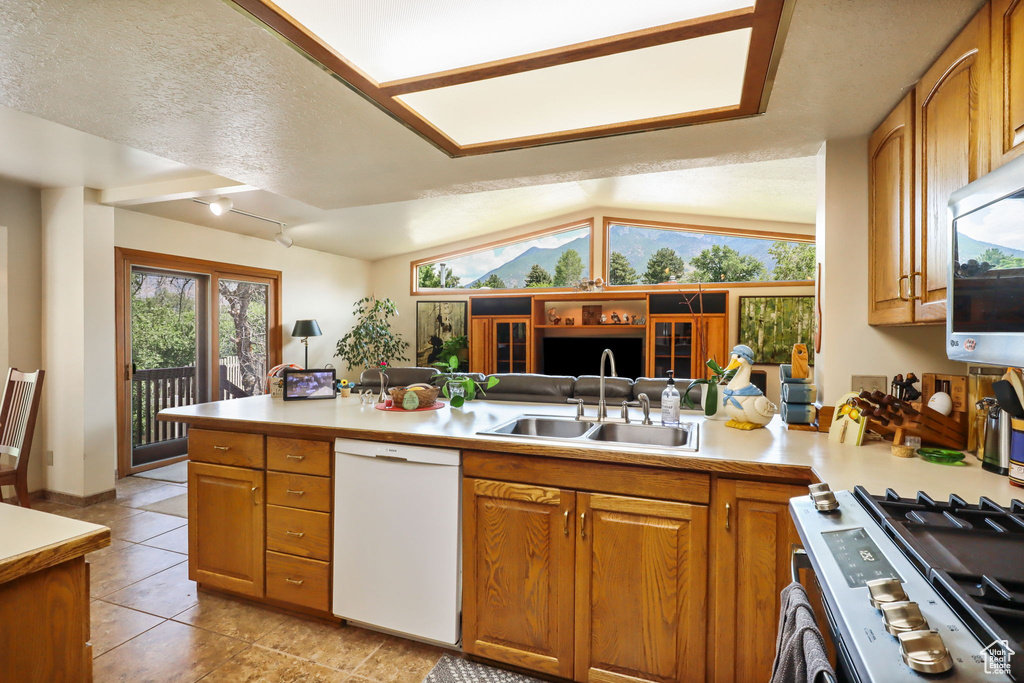 Kitchen with appliances with stainless steel finishes, light countertops, brown cabinets, a peninsula, and light tile patterned flooring