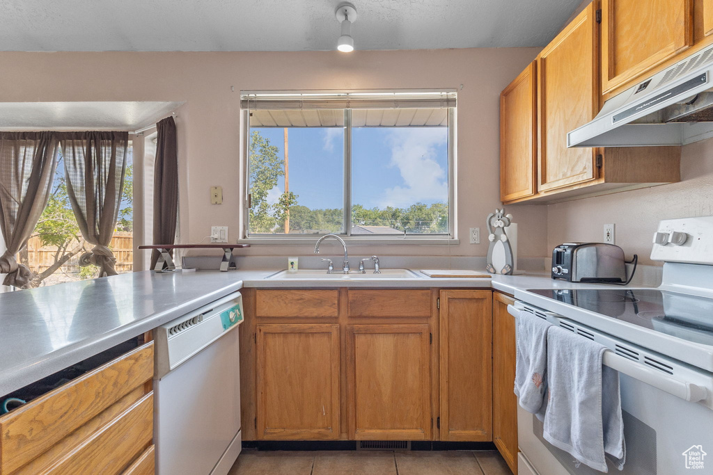 Kitchen featuring white appliances, under cabinet range hood, light tile patterned floors, light countertops, and brown cabinets