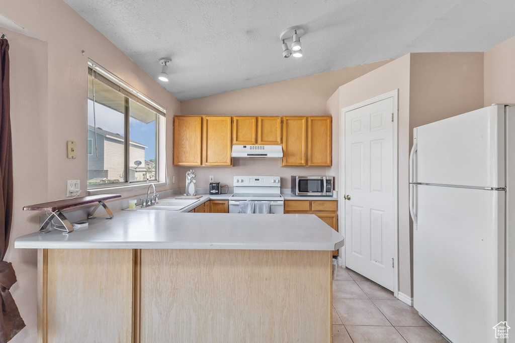Kitchen with white appliances, under cabinet range hood, a peninsula, lofted ceiling, and light countertops