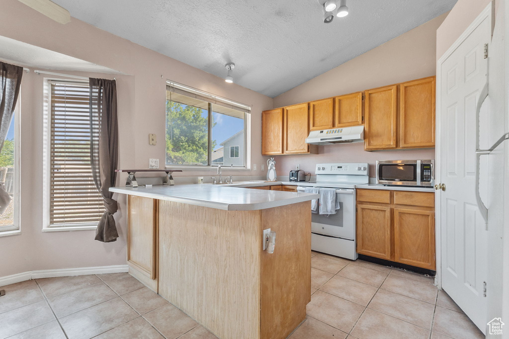 Kitchen featuring white range with electric stovetop, stainless steel microwave, under cabinet range hood, a peninsula, and light tile patterned floors