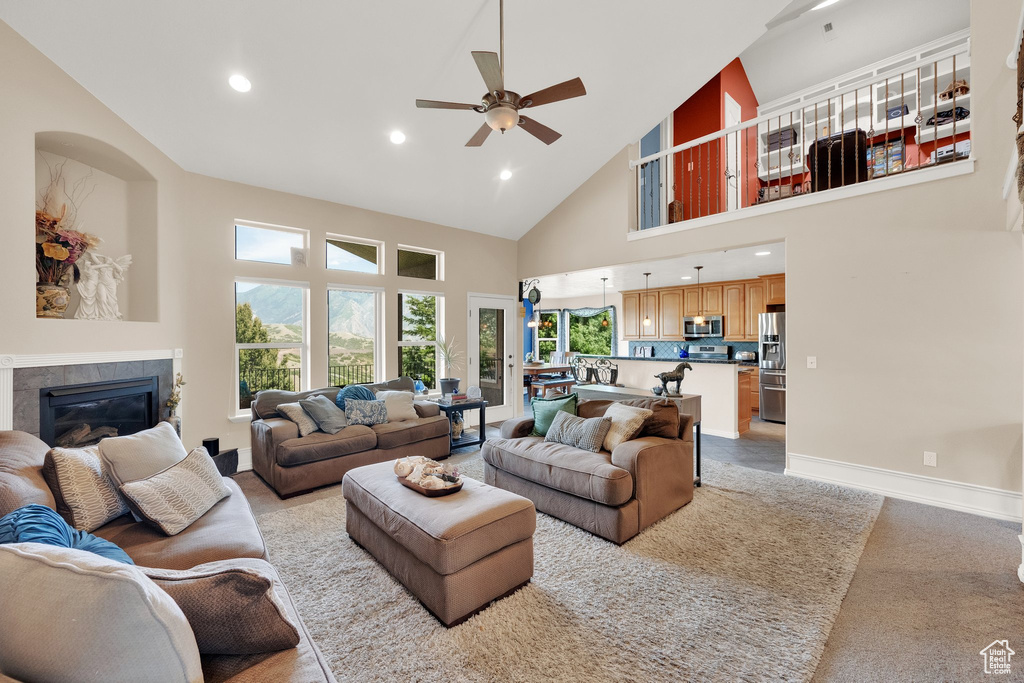 Living room with high vaulted ceiling, recessed lighting, a ceiling fan, a glass covered fireplace, and light colored carpet