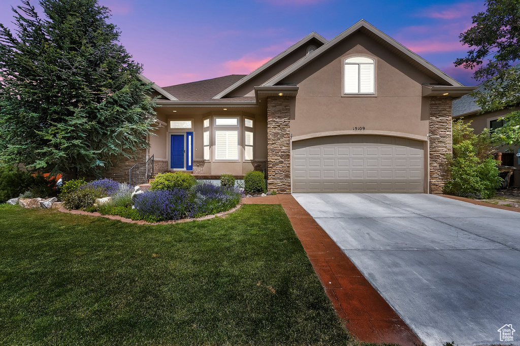 View of front of property with stone siding, stucco siding, concrete driveway, a lawn, and roof with shingles