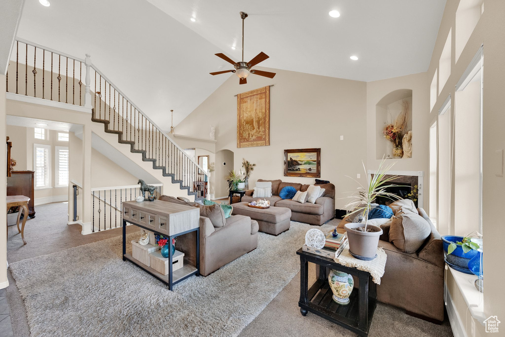 Carpeted living room with arched walkways, high vaulted ceiling, ceiling fan, recessed lighting, and stairway