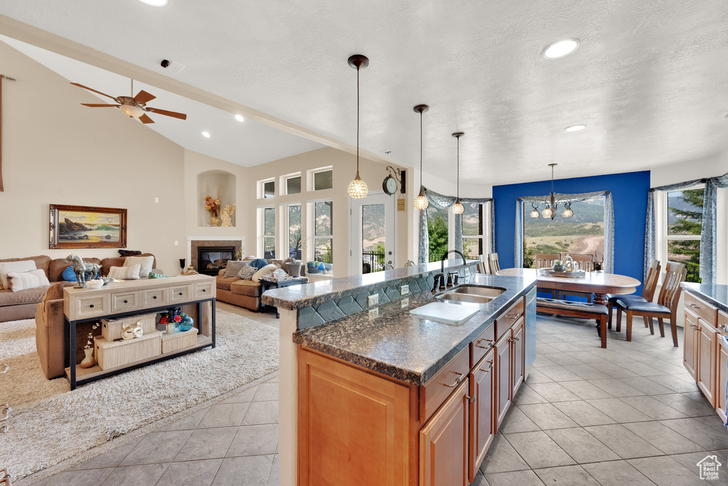 Kitchen featuring a glass covered fireplace, recessed lighting, dark stone countertops, a center island with sink, and lofted ceiling