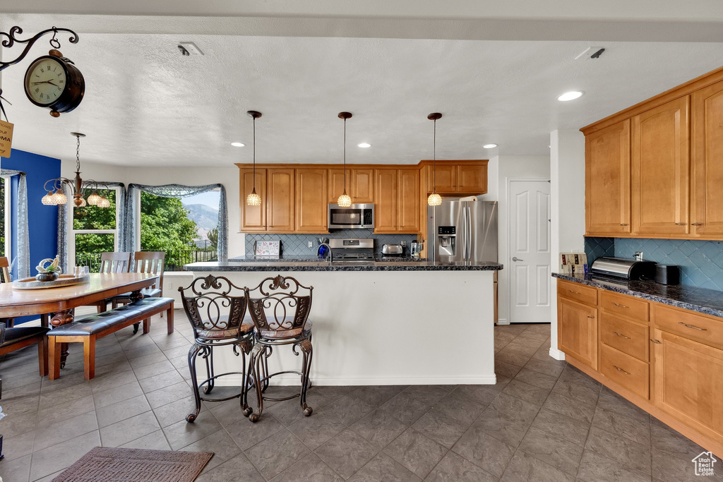 Kitchen with appliances with stainless steel finishes, backsplash, a kitchen breakfast bar, recessed lighting, and hanging light fixtures
