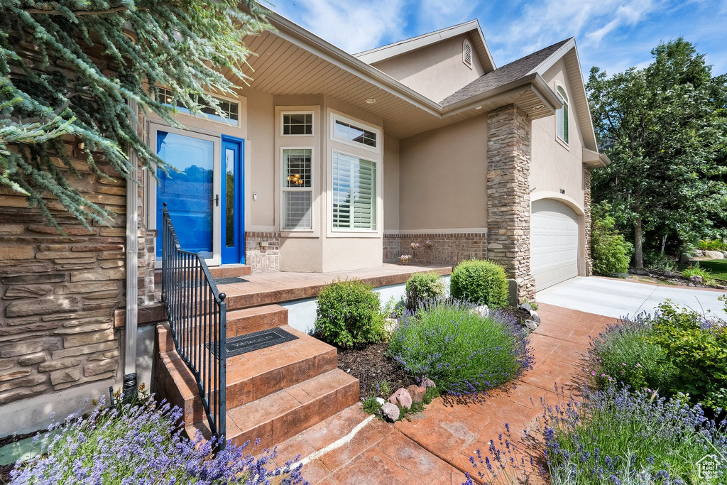 View of exterior entry with stucco siding, stone siding, concrete driveway, and an attached garage