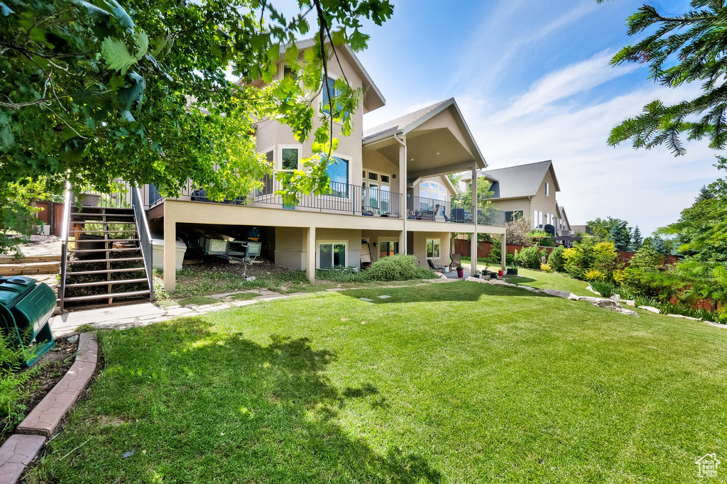 Rear view of property with stucco siding, a lawn, and stairs