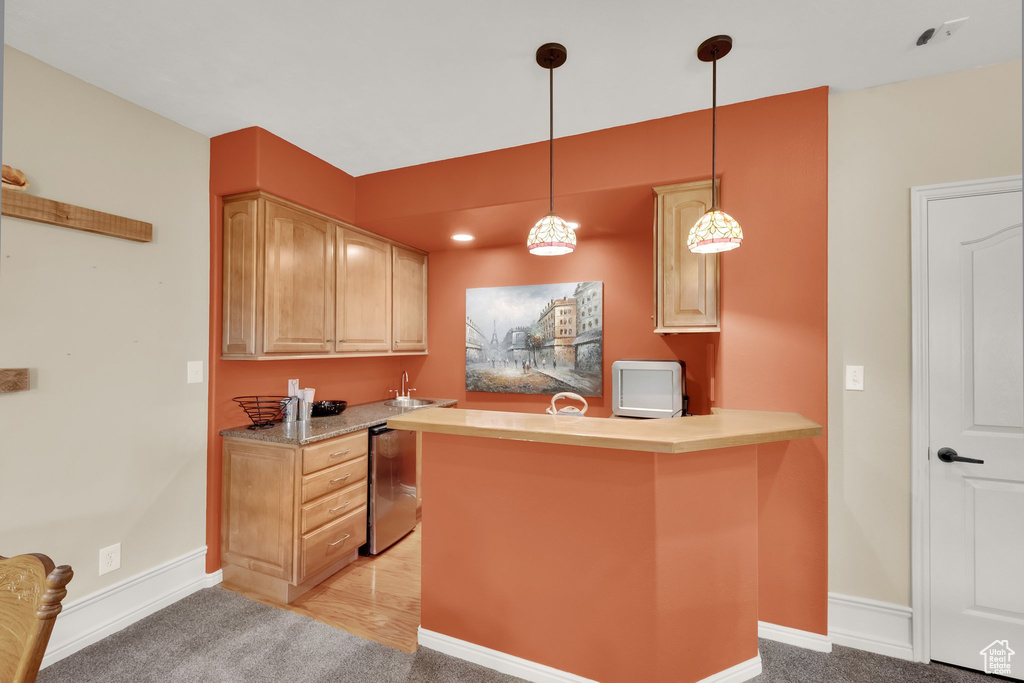 Kitchen with a peninsula, pendant lighting, light countertops, light colored carpet, and light brown cabinetry