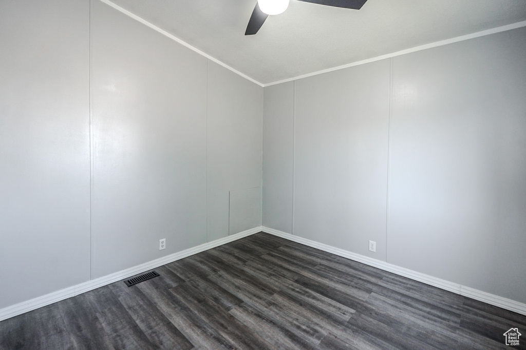 Spare room featuring a ceiling fan, dark wood finished floors, vaulted ceiling, a decorative wall, and ornamental molding