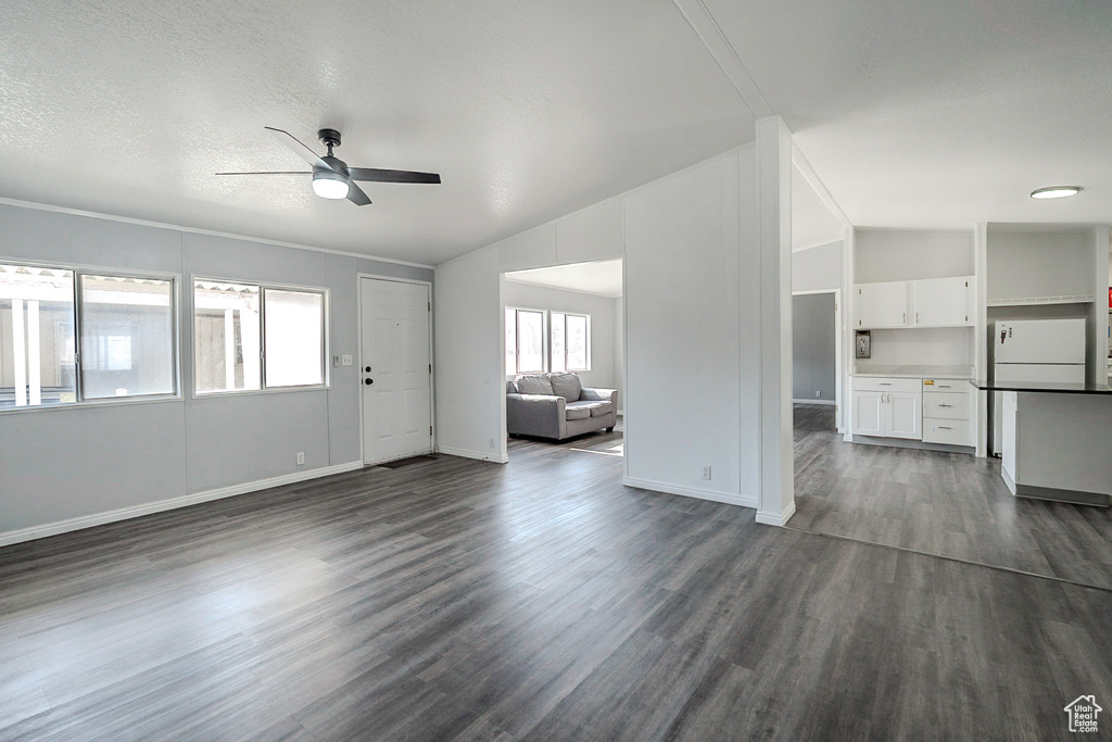Unfurnished living room featuring a ceiling fan, vaulted ceiling, and dark wood finished floors