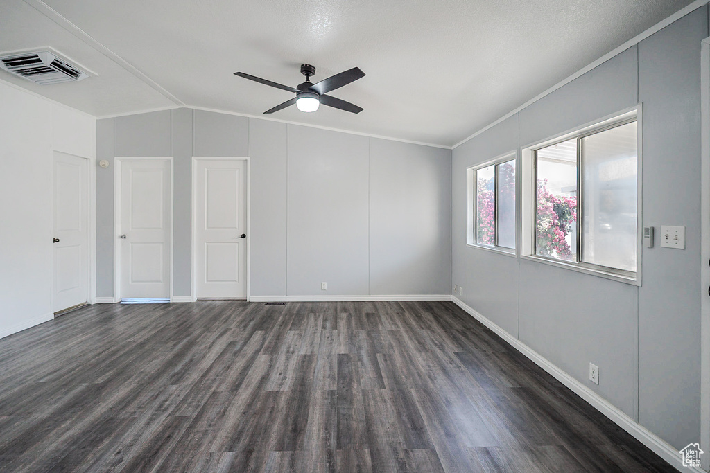 Spare room featuring dark wood-style flooring, vaulted ceiling, ceiling fan, and crown molding