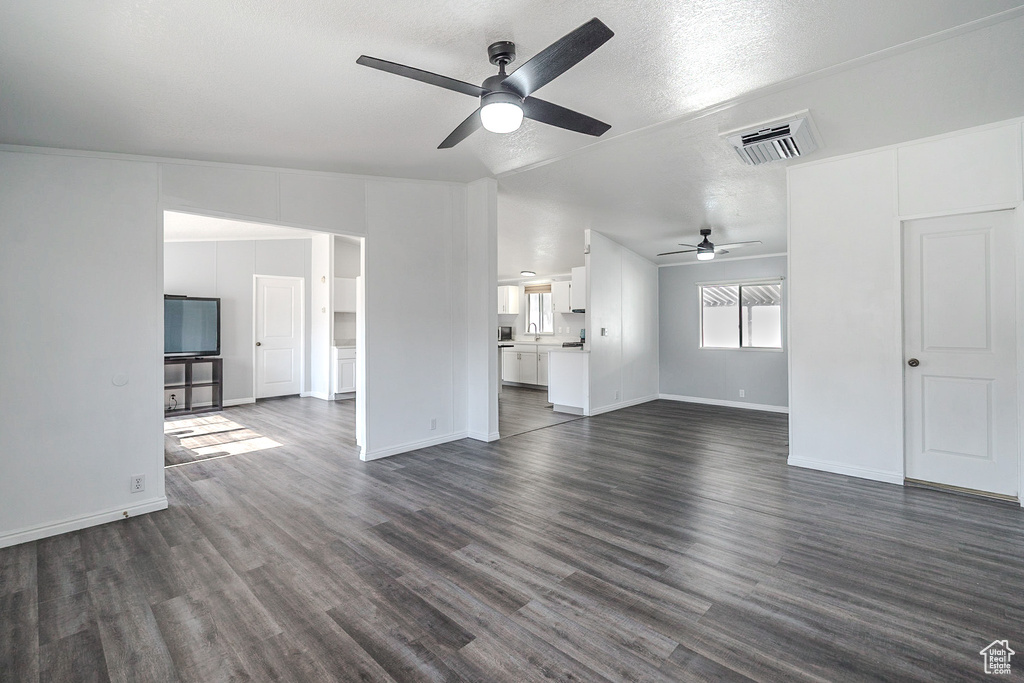 Unfurnished living room with ceiling fan, dark wood-style flooring, and a textured ceiling