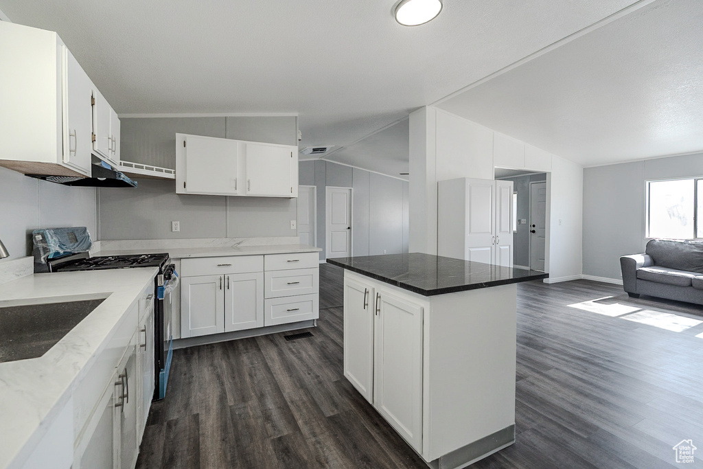 Kitchen with stainless steel range with gas cooktop, dark wood finished floors, open floor plan, white cabinetry, and vaulted ceiling