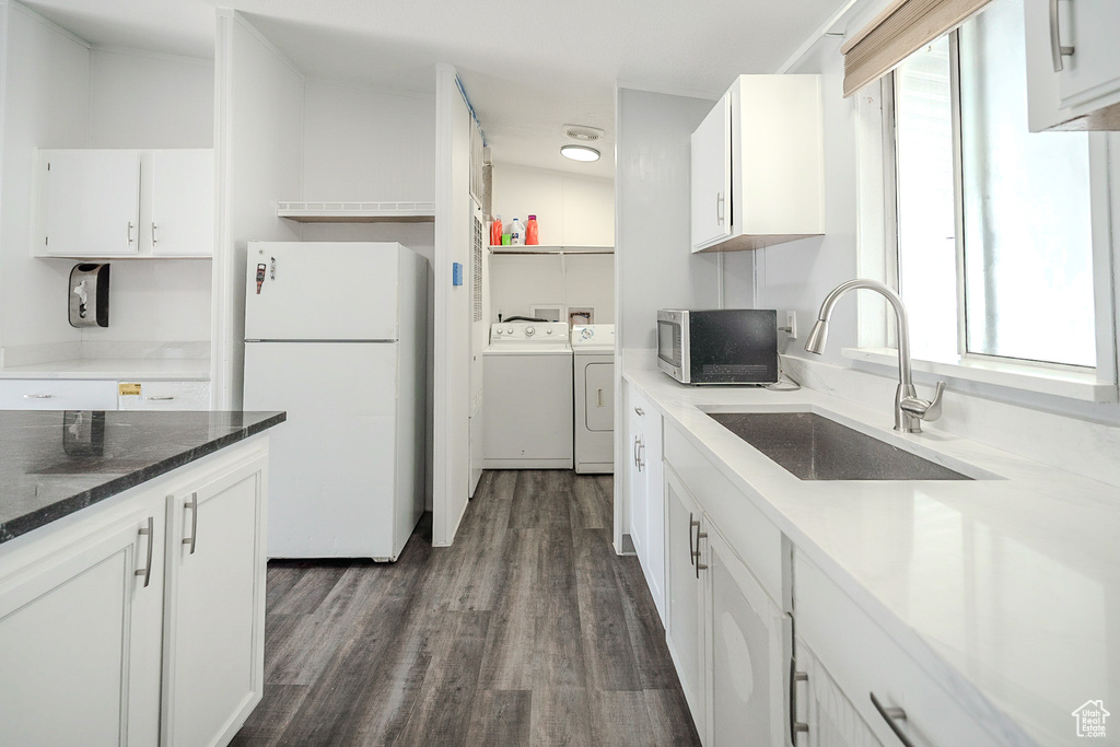 Kitchen featuring freestanding refrigerator, washing machine and dryer, stainless steel microwave, dark wood finished floors, and healthy amount of natural light