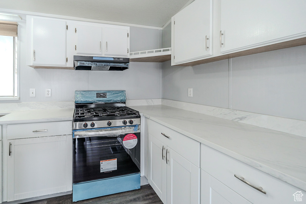 Kitchen featuring stainless steel gas range, range hood, white cabinets, light countertops, and plenty of natural light