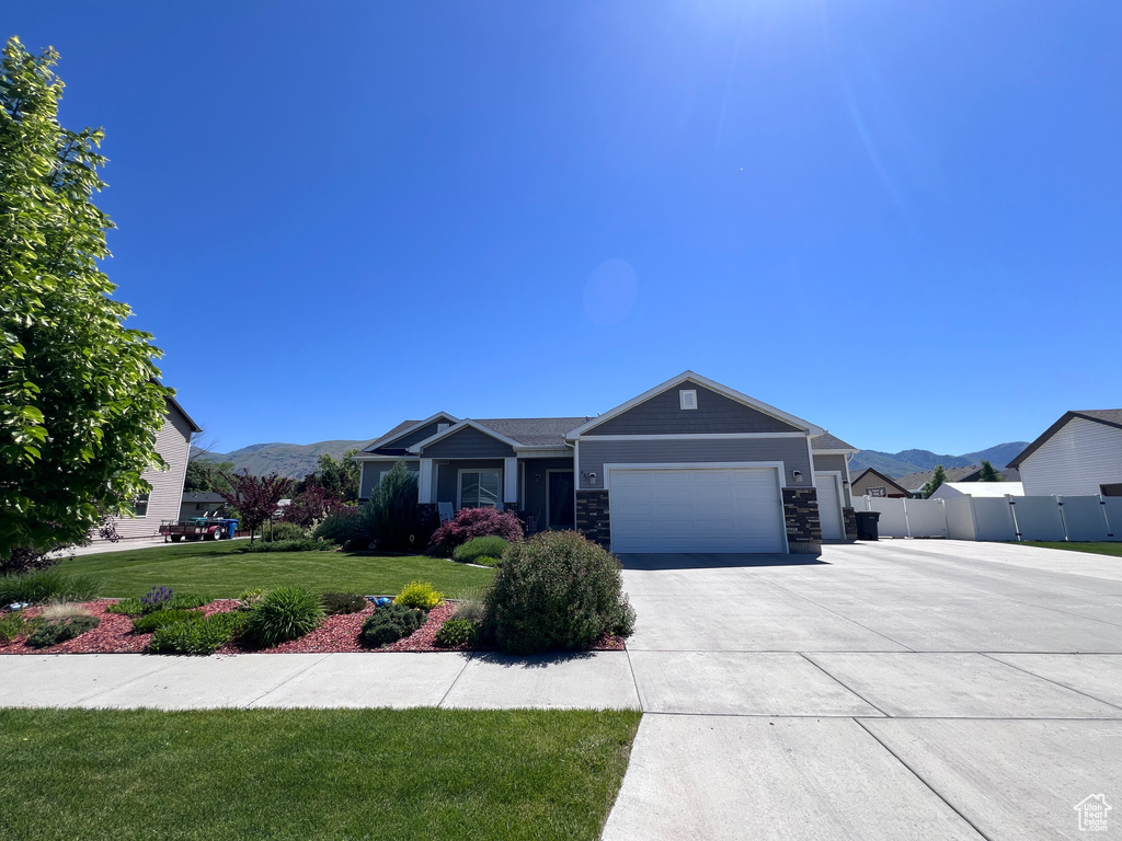 View of front facade featuring an attached garage, a mountain view, concrete driveway, and stone siding