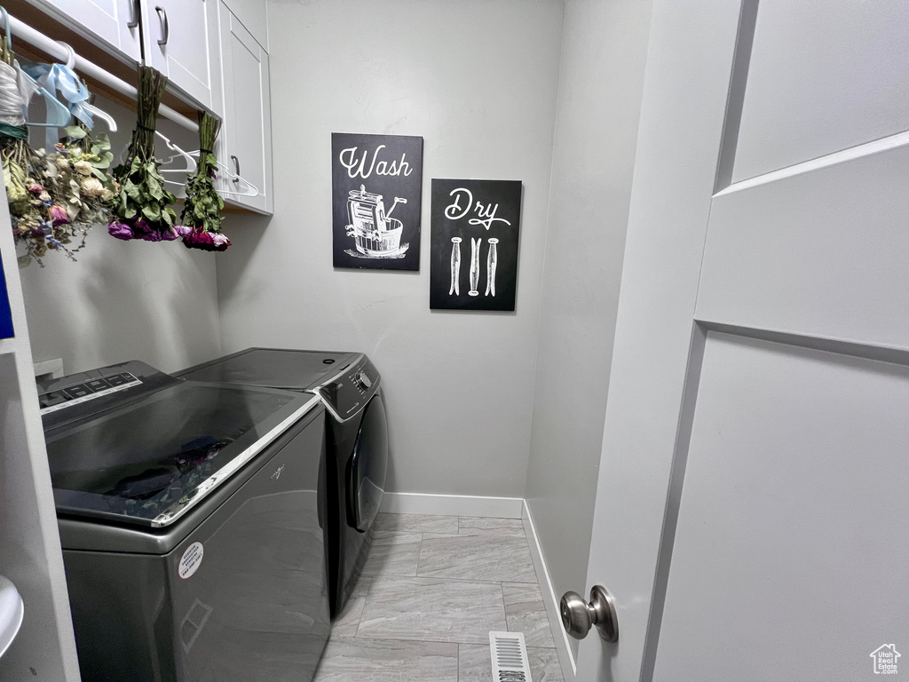 Laundry area featuring independent washer and dryer, cabinet space, and light marble finish floors