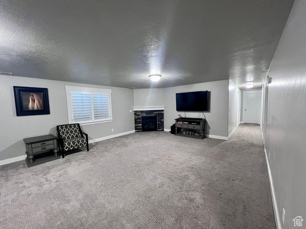 Unfurnished living room featuring a textured ceiling, carpet floors, and a stone fireplace